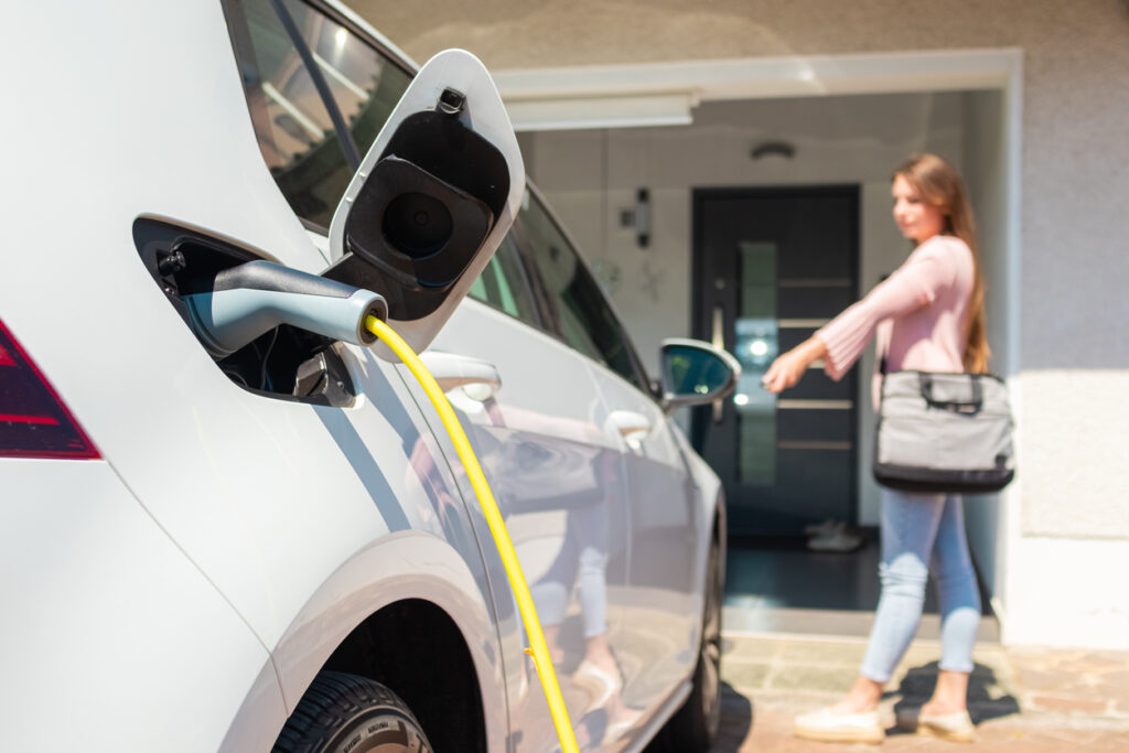 Woman charging electric car at home with cable.